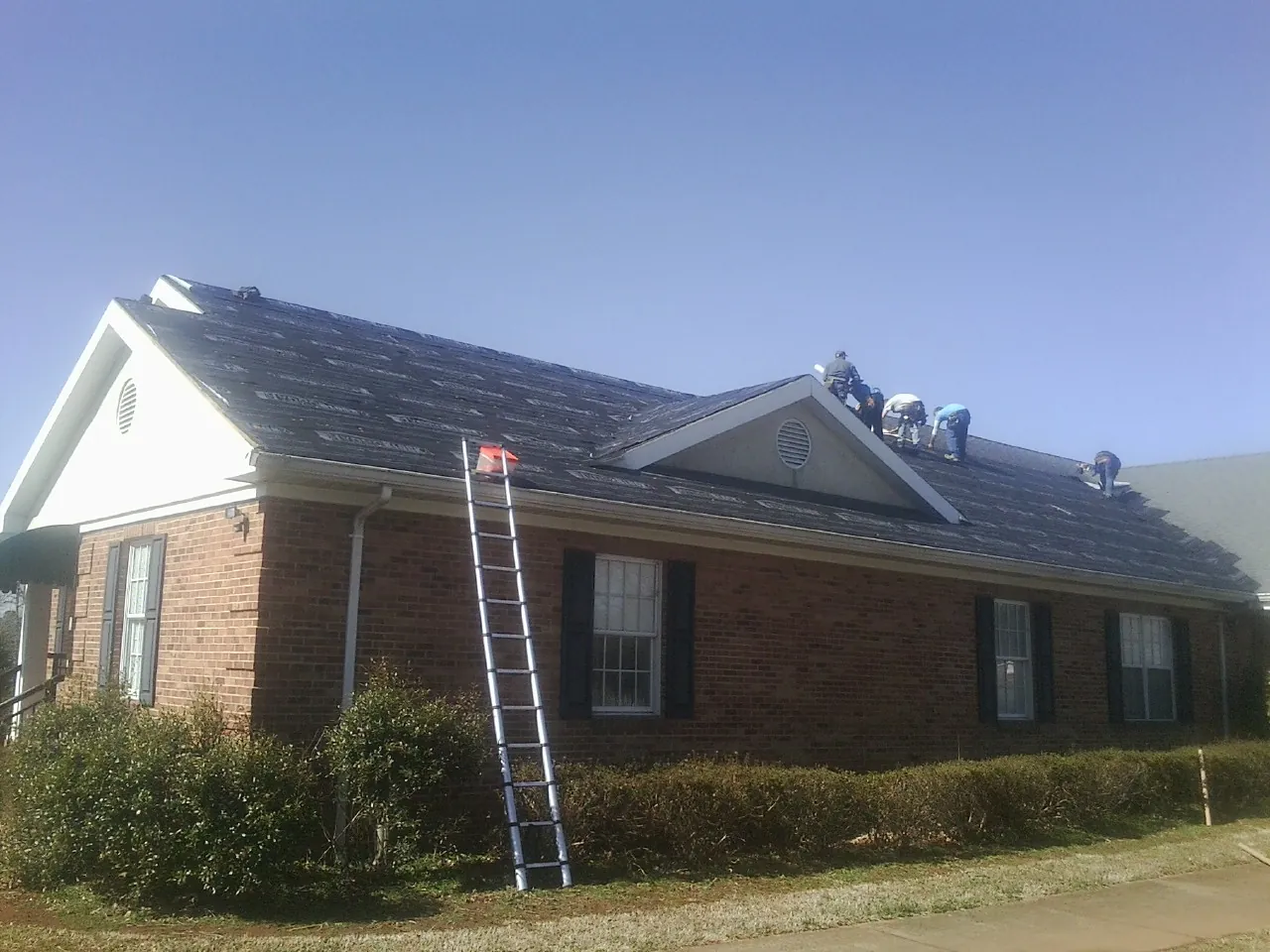 Crew tearing shingles off a brick ranch roof with a ladder set — Metal Roof Repair work by our crew in Russellville