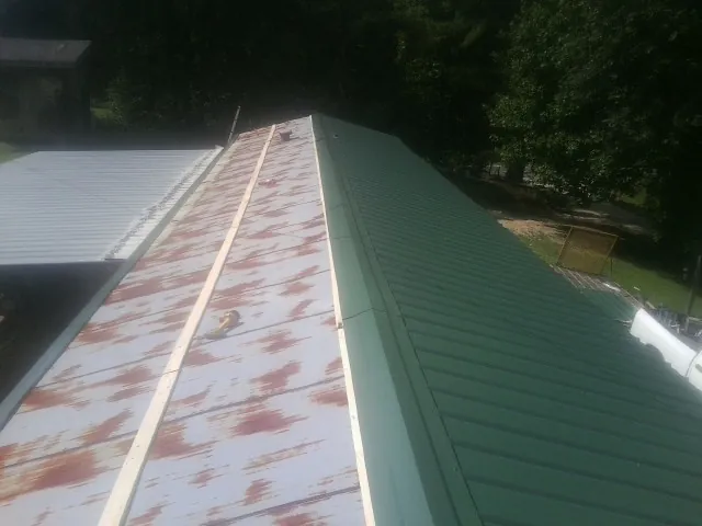 Old rusted panels beside newly installed green metal roofing — Wind Damage Roof Repair by Roofing Brothers in Russellville